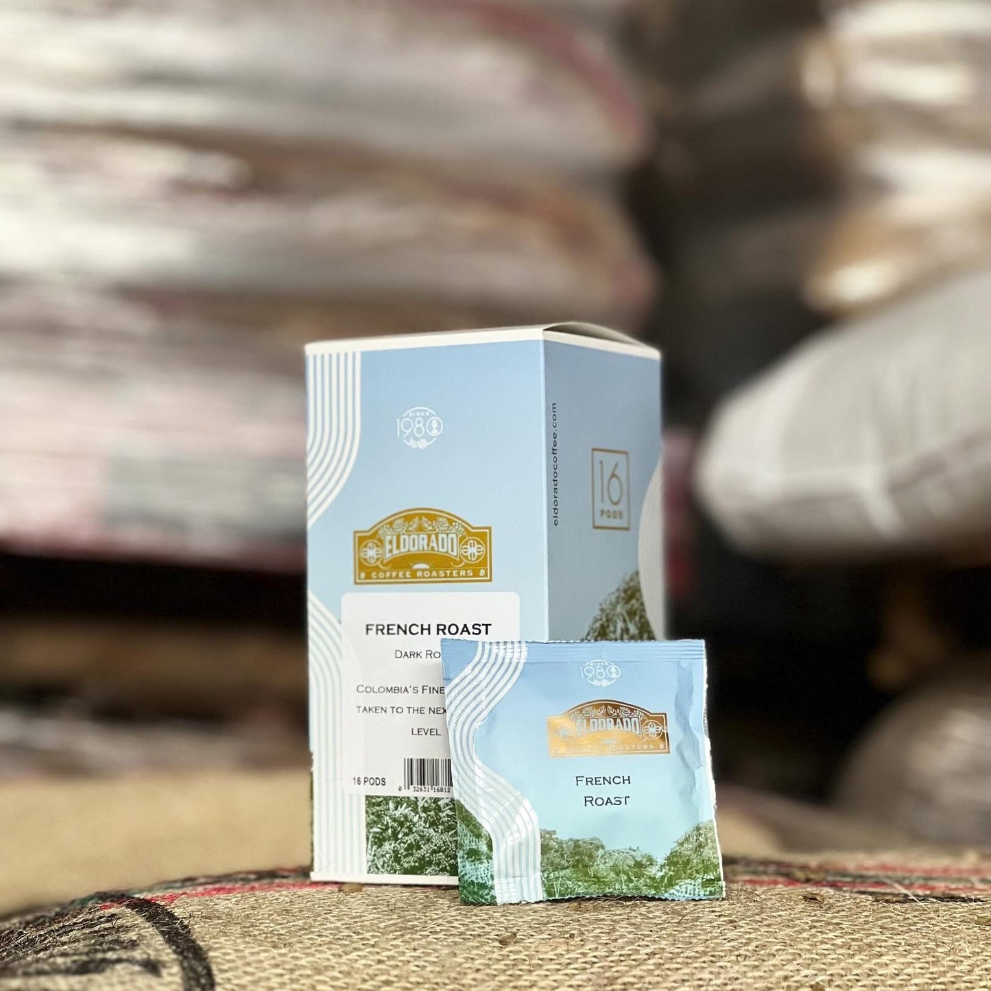 A box of El Dorado Coffee Roasters French Roast coffee pods sits on a burlap sack. One single-serve pod leans against the box, showcasing the brand's packaging.