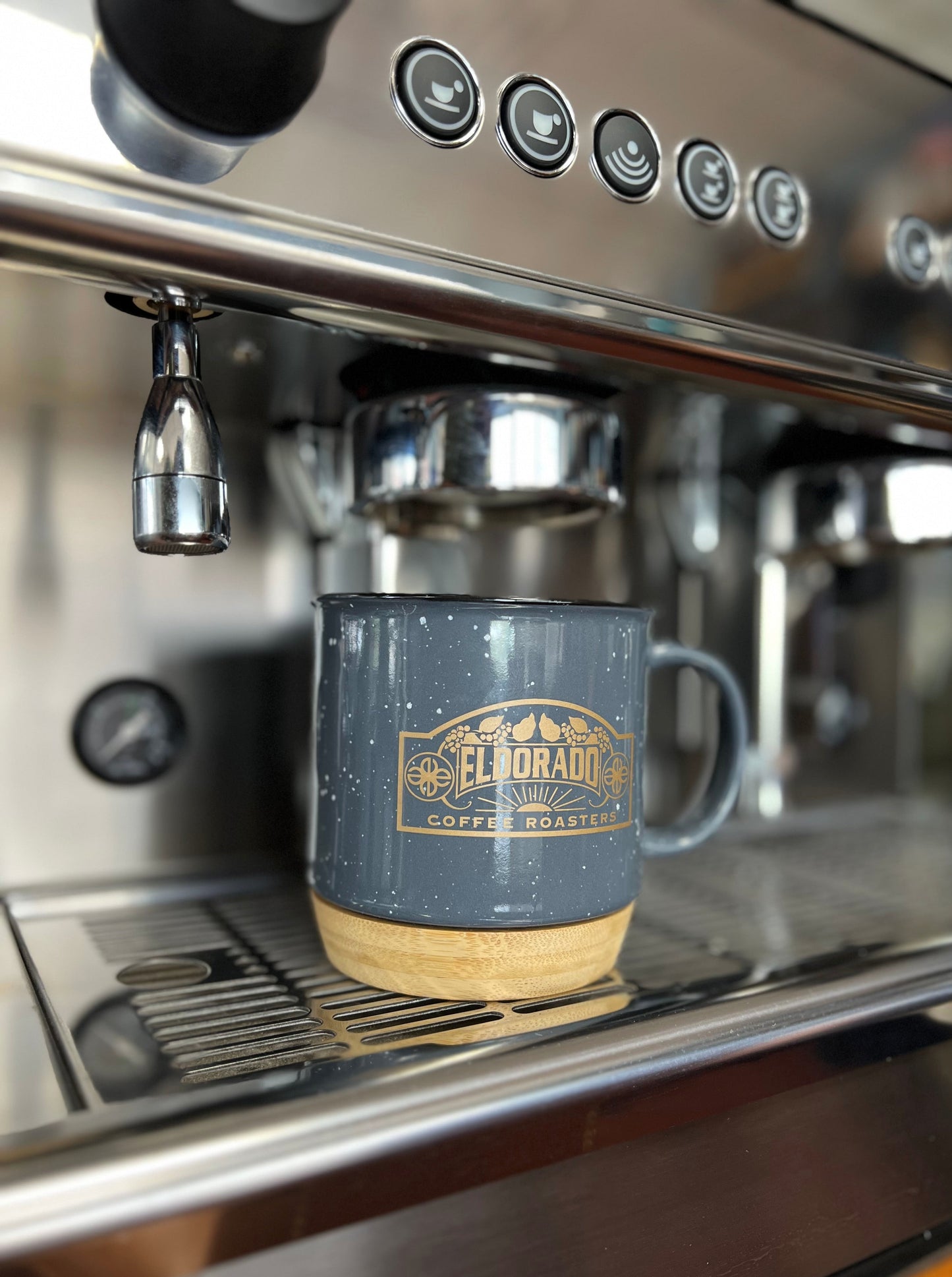 A speckled gray Eldorado Coffee Roasters mug sits on the warming tray of an espresso machine, ready to be filled.