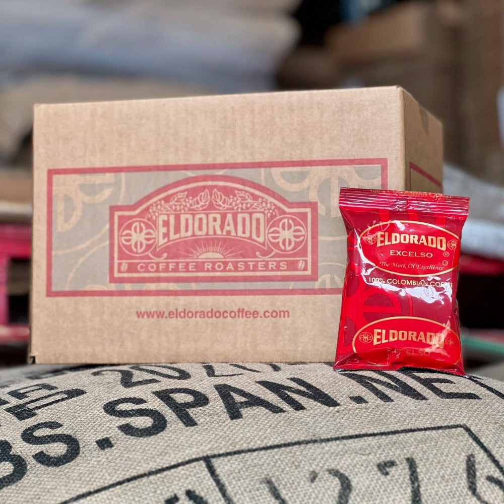 Eldorado Coffee Roasters box sits atop a burlap coffee bean bag with a single bag of Eldorado Excelso 100% Colombian coffee leaning against it.
