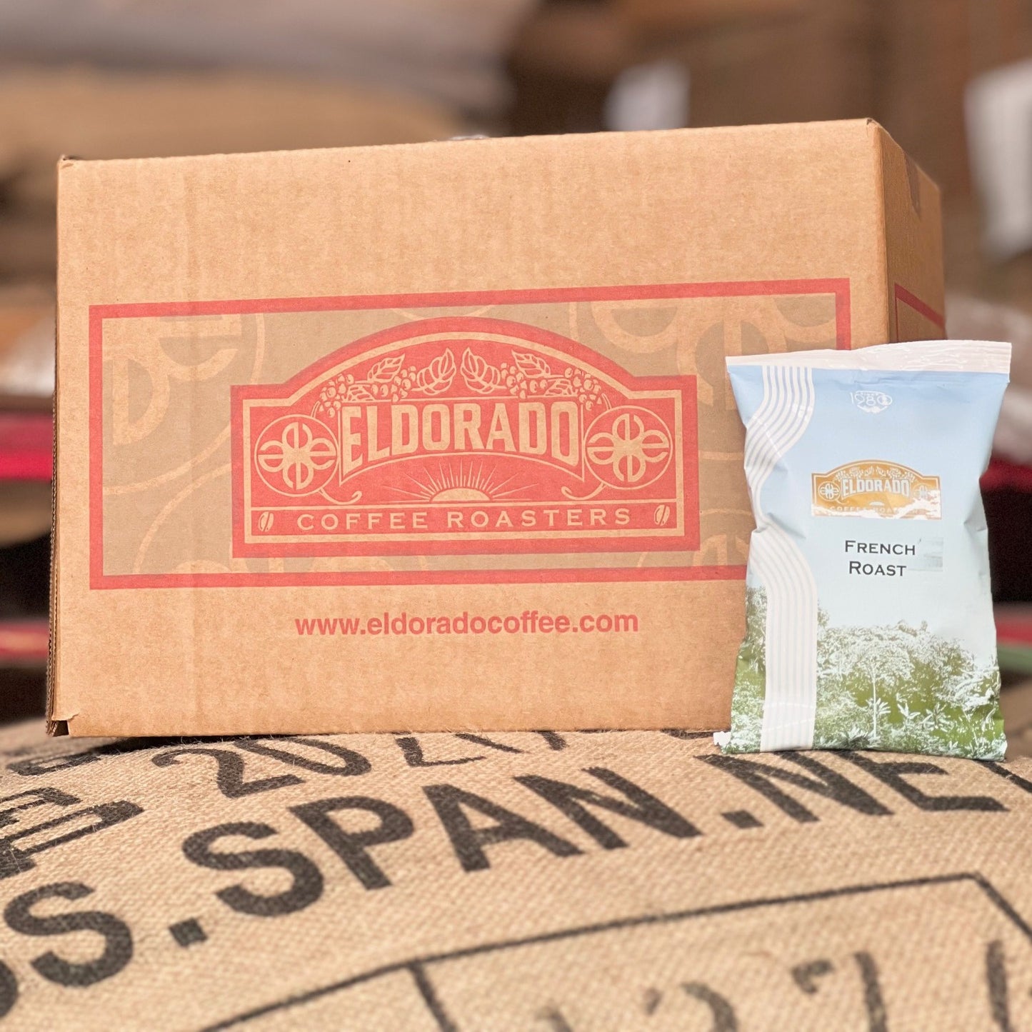 A cardboard box of Eldorado Coffee Roasters sits atop a burlap coffee bean sack, with a bag of French Roast coffee leaning against the box.
