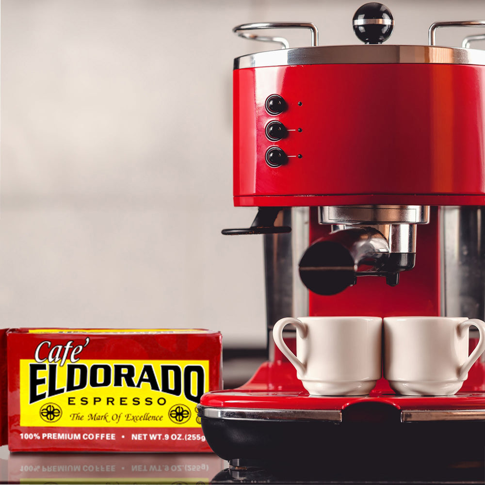 A red espresso machine brews a fresh cup of Cafe Eldorado coffee, two white espresso cups await.