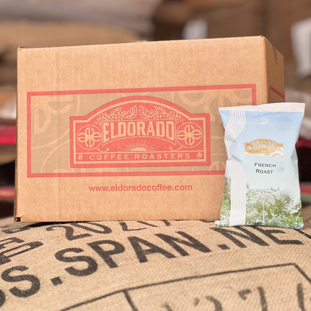 Cardboard box filled with El Dorado Coffee Roasters French Roast coffee rests on a burlap coffee bean bag. 
